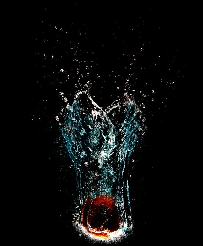 A red apple creating a splash in water against a black background, showcasing dynamic motion.