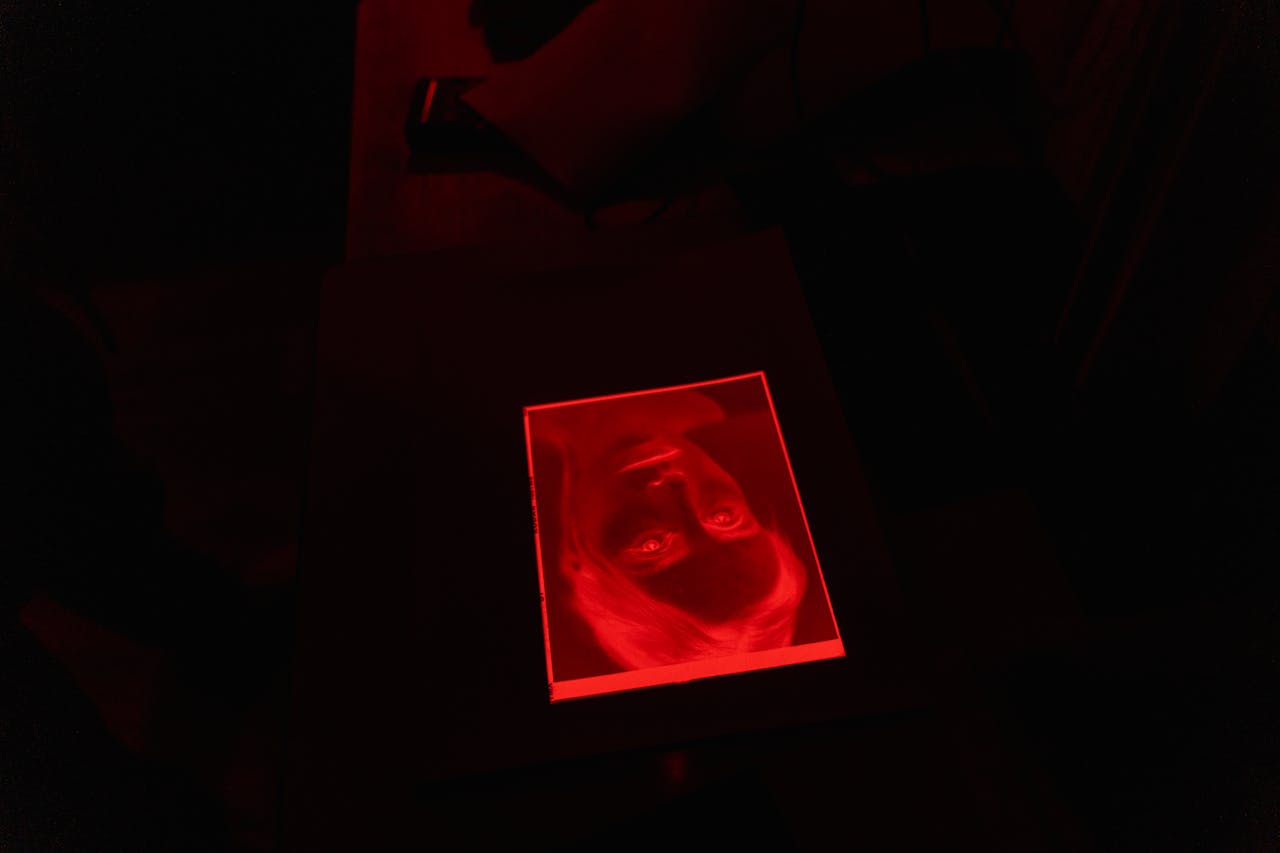 A red-tinted photograph lies on a black surface in a dark room, creating a mysterious ambiance.